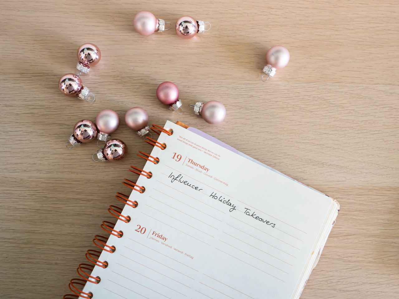 Open planner with Christmas baubles on wooden surface. Perfect for holiday planning themes.